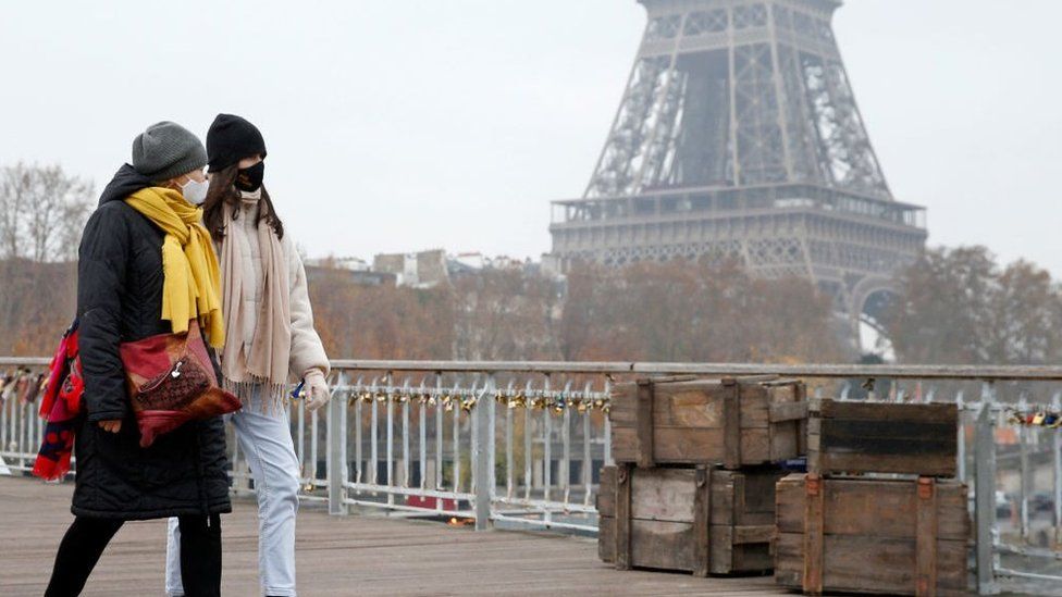 Women walk in front of the Eiffel Tower wearing Covid face masks, November 2021