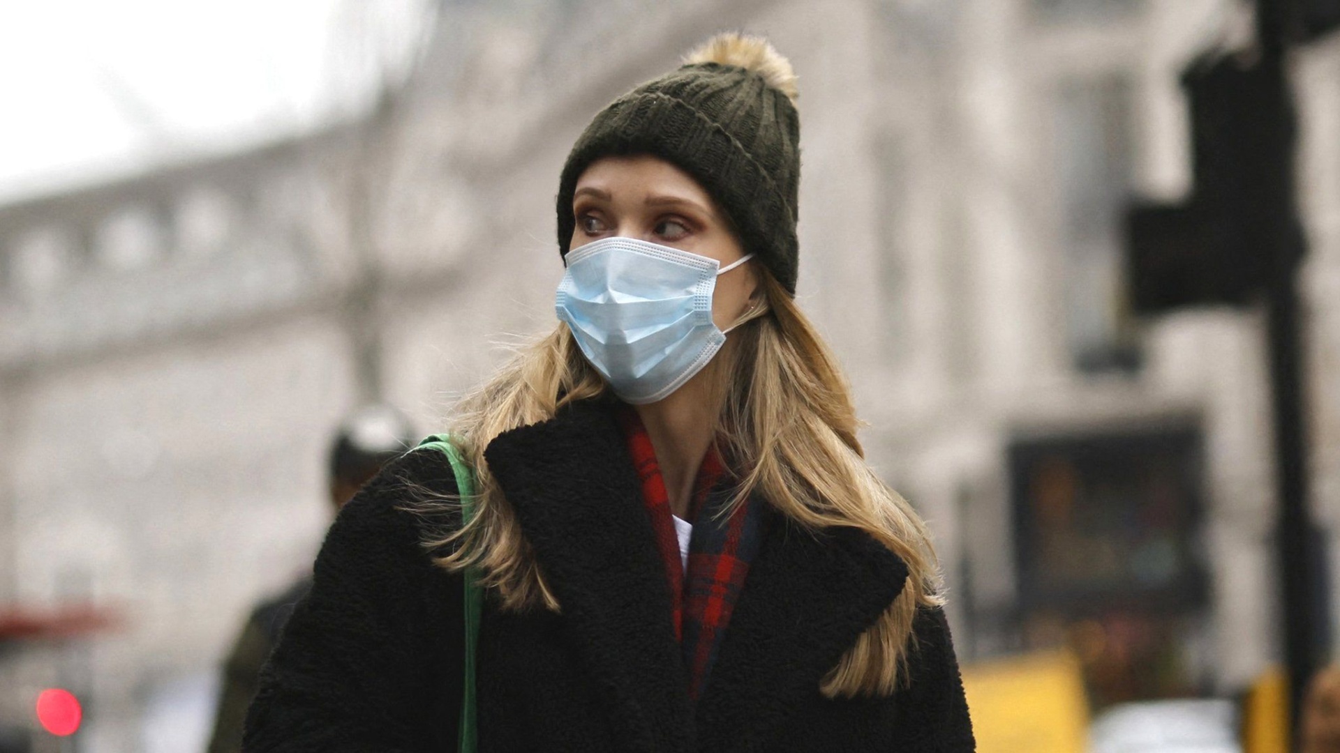 A woman in a mask walks down a street in London