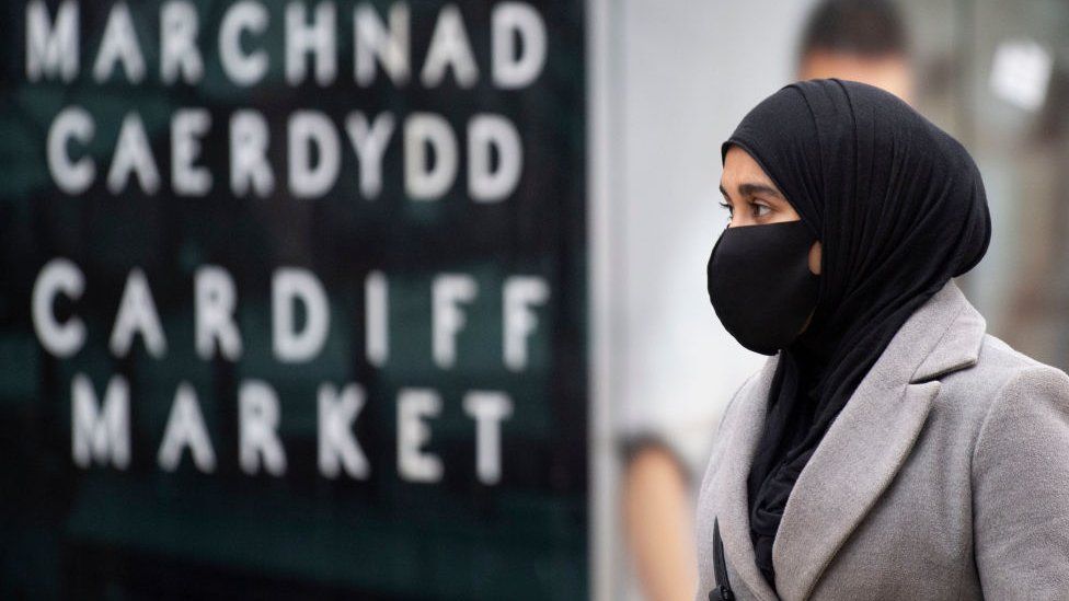 Woman walks by Cardiff market sign, wearing face mask