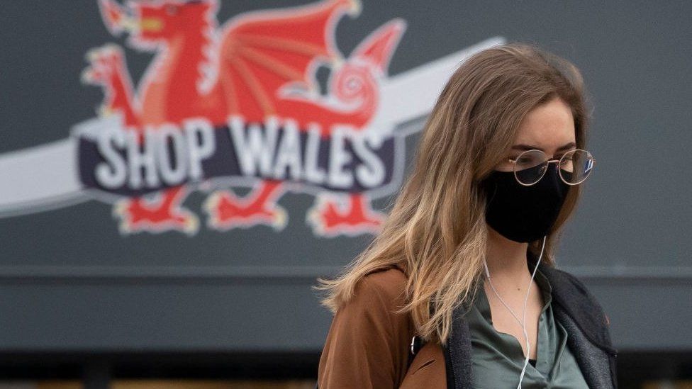 Woman in face mask with dragon on shop behind her in Cardiff