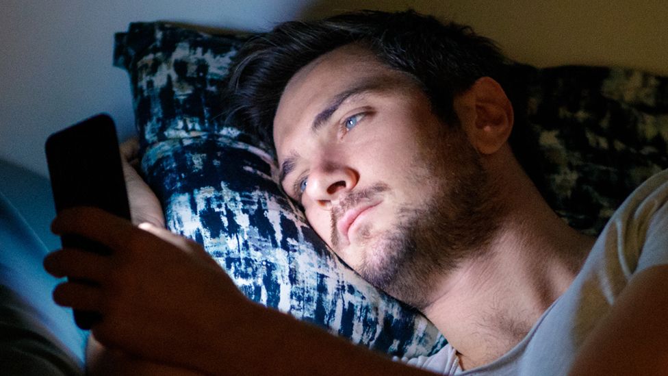 Stock image of a man lying in bed using a smartphone