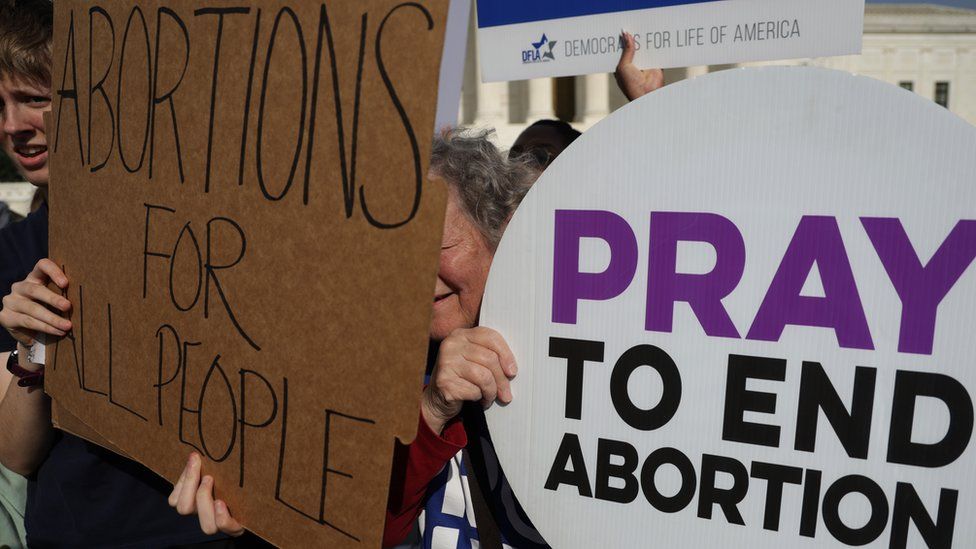 protests signs read 'pray to end abortion' and 'abortions for all people'