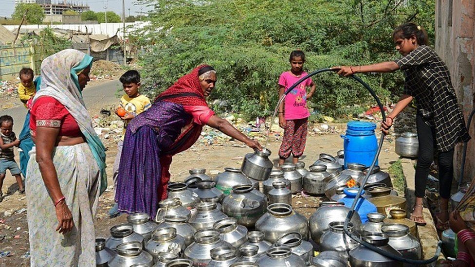 A woman pours drinking water in a pot offered by a temple in the vicinity on a hot summer day on the outskirts of Ahmedabad