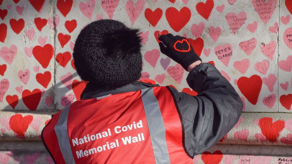 A volunteer paints red hearts on the National Covid Memorial Wall in Westminster