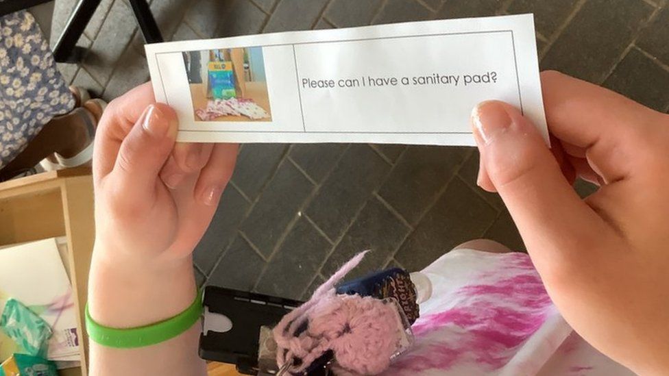 Photo shows student holding a slip that says 'please can I have a sanitary pad?' next to a photo of some pads. The student is handing it in to reception.