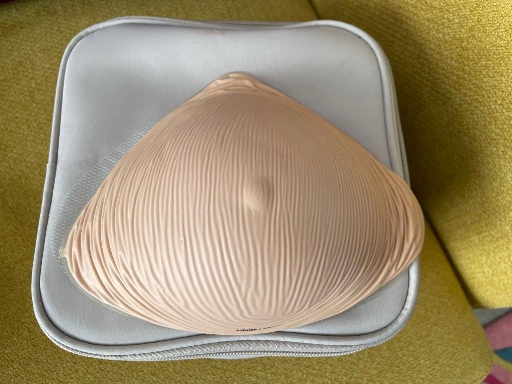A pale skinned prosthetic breast, on top of the case it's stored in.