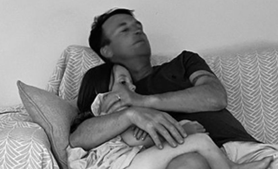 Hollie's husband Mike cuddling Sydney on the sofa. The photo has a black and white treatment.