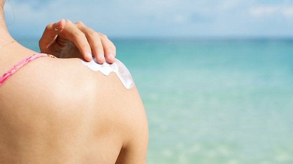 A woman applies sunscreen to her shoulder