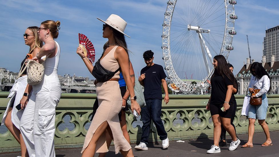 People walk along Westminster bridge on 3 September, image shows a group of mixed gender people, one of them fanning themselves to cool down from the heat.