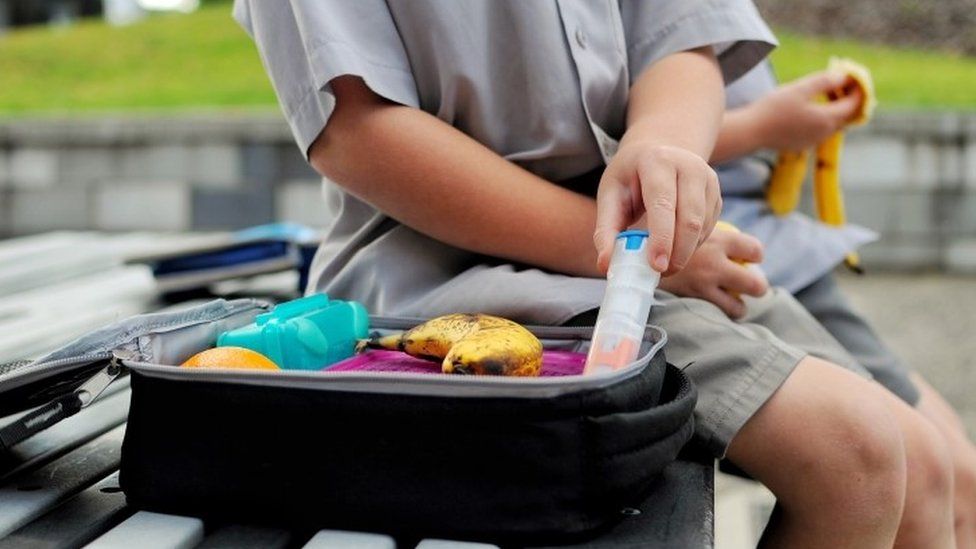 Young boy with a packed lunch takes out his anaphylaxis auto injector