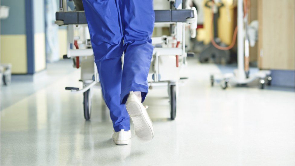 Legs of medic running with gurney along hospital corridor - stock photo